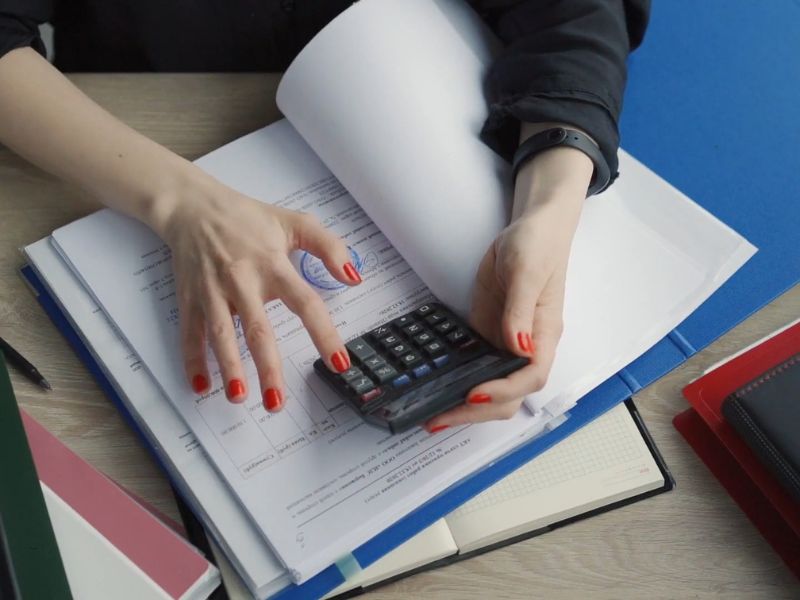 osoba iz poreske kontrole proverava papire i koristi kalkulator