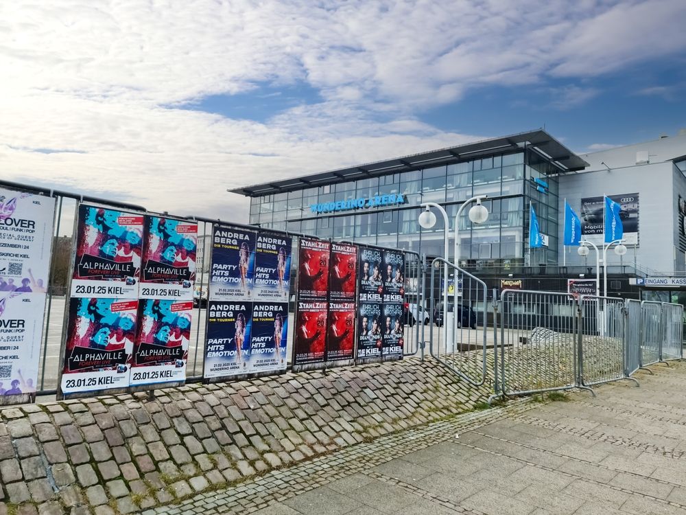 Reklamni plakati postavljeni na ogradi ispred javnog objekta u urbanom prostoru.
