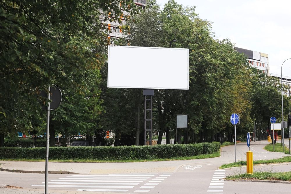bord postavljen pored pešačke staze i saobraćajnice u urbanom okruženju.